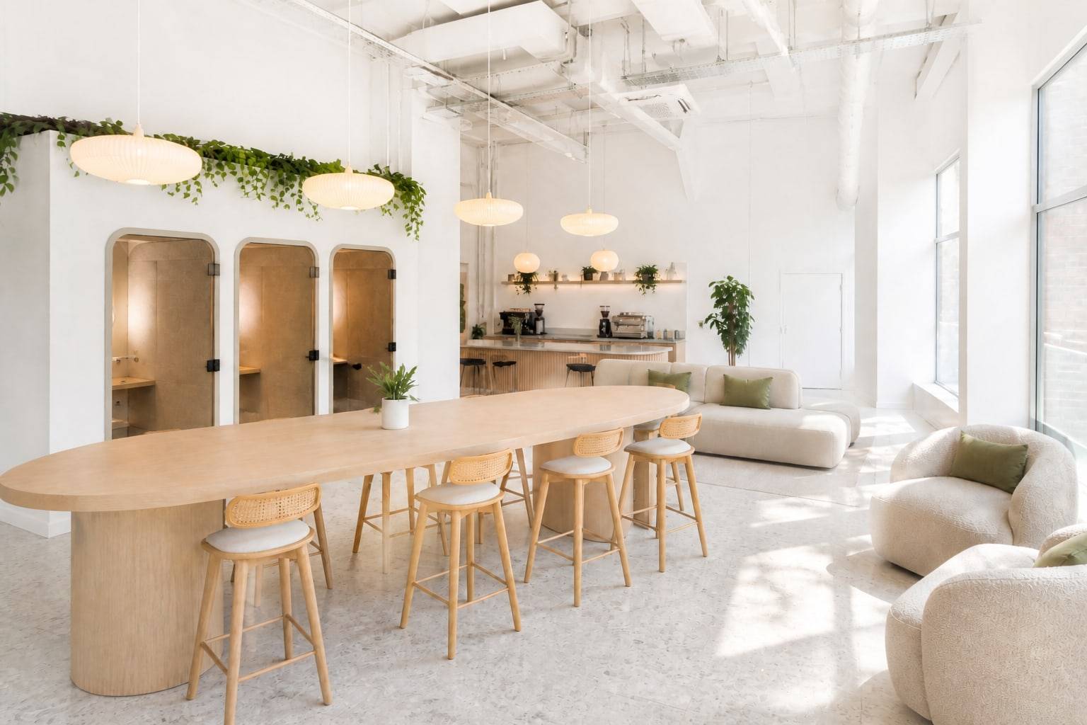 Bright coworking lounge with a communal oak table, cream seating, and arched booths